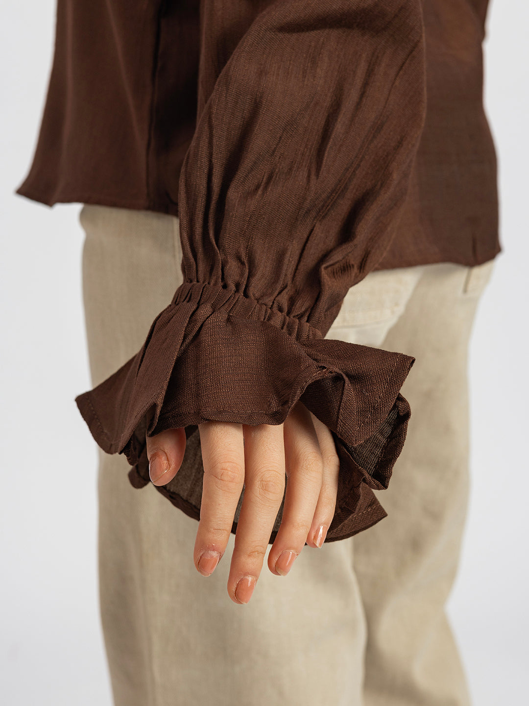 Styling shot of brown ruffled cuff shirt tucked into trousers