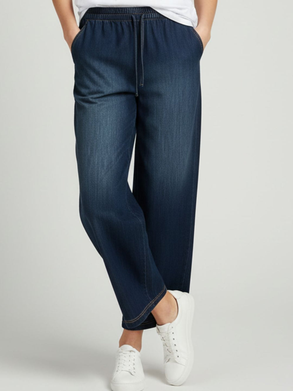 Side angle of dark blue denim trousers showing mid-rise drawstring waist
