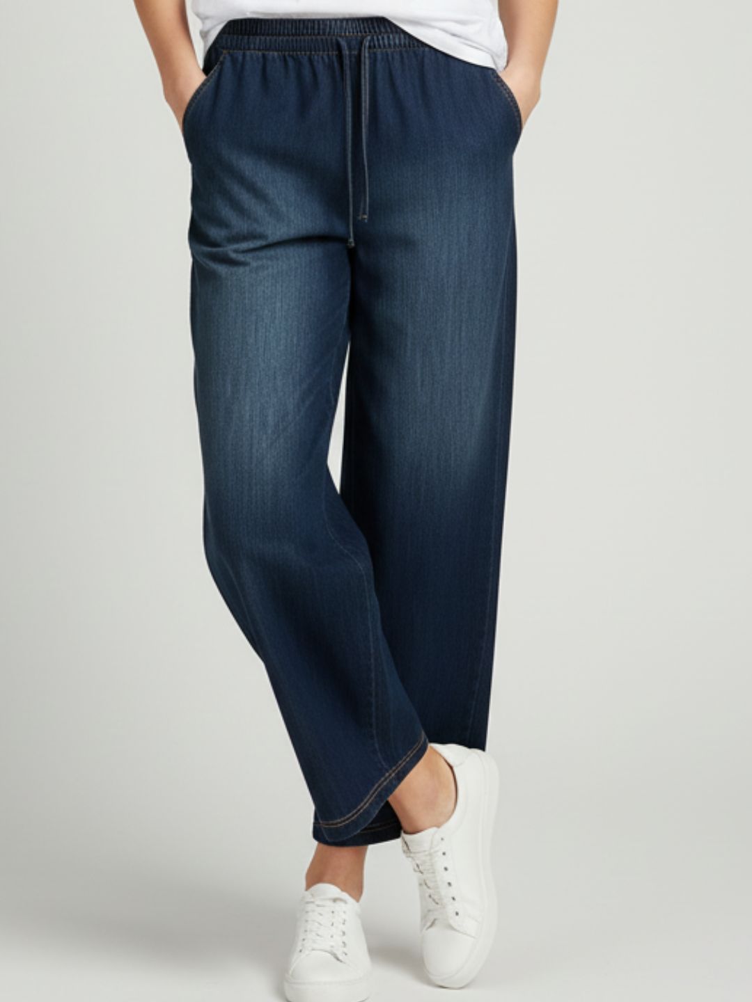 Side angle of dark blue denim trousers showing mid-rise drawstring waist