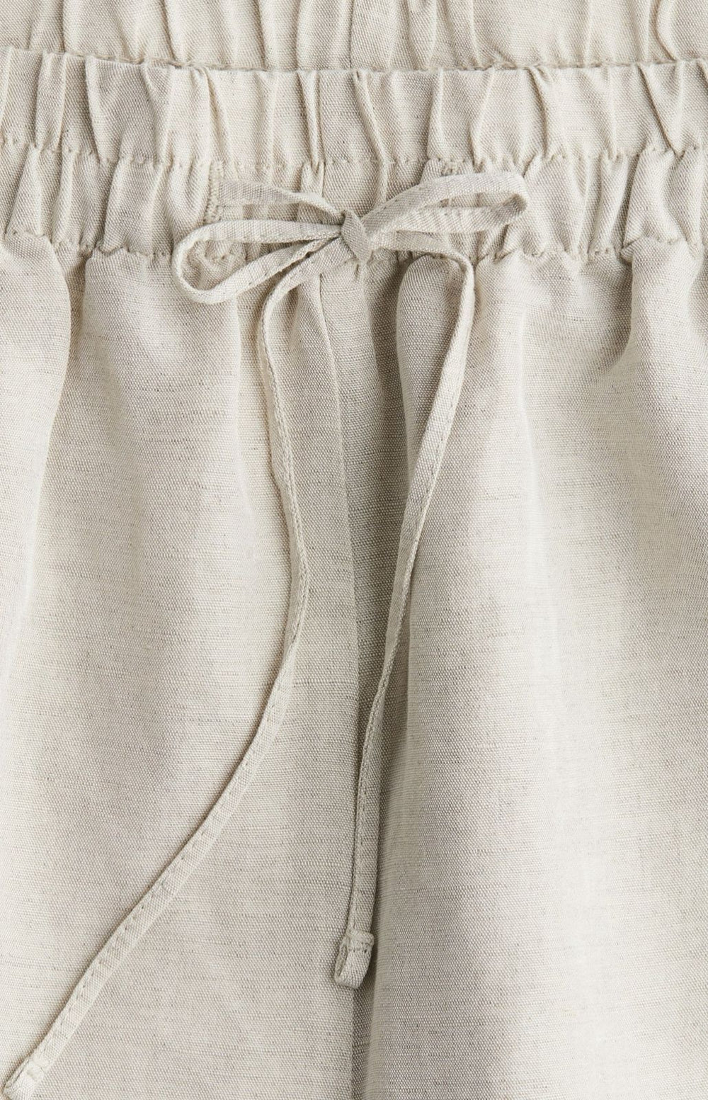 Side view of off-white baggy trousers with drawstring waist