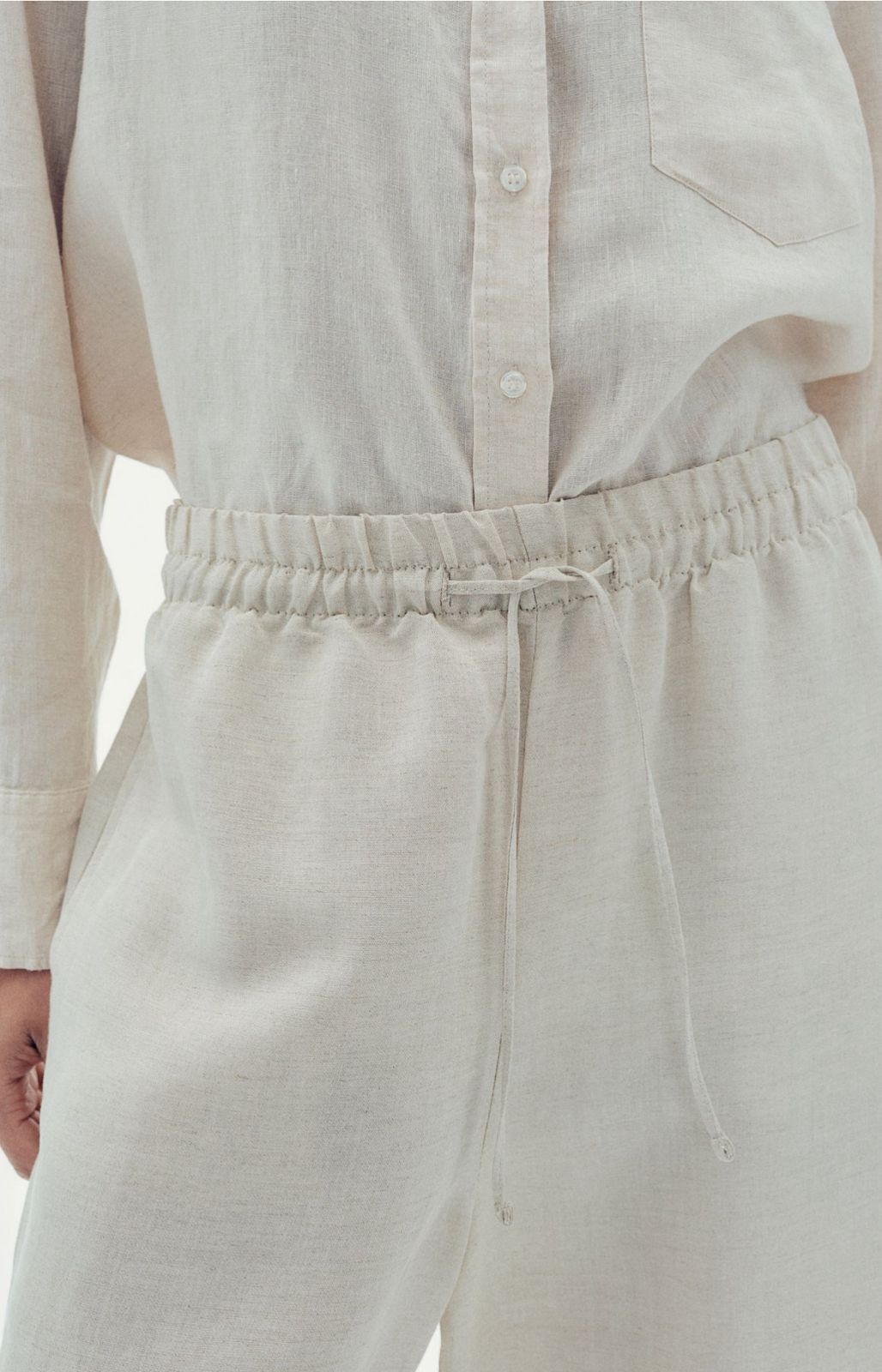 Detail of elasticated drawstring waist on off-white trousers